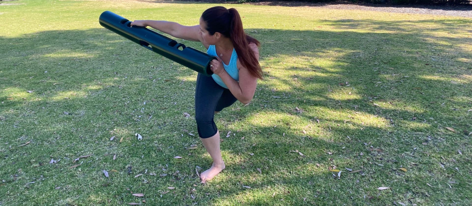Personal training outdoors in a park, working through a rotational lunge with a weighted tube